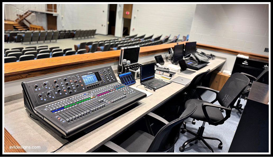 Audio mixing console on a workstation in a control booth overlooking an empty auditorium. (Theatre control room)