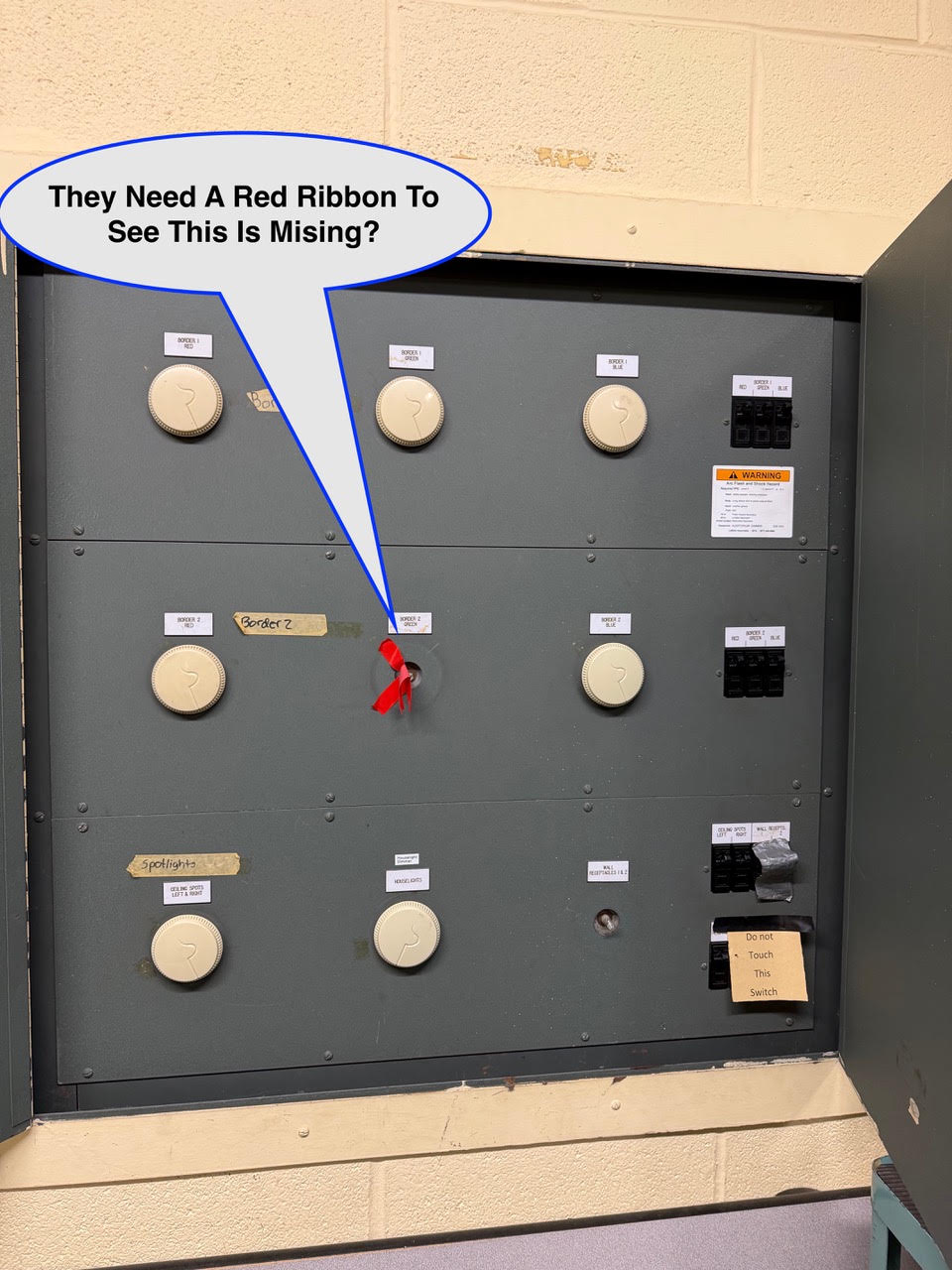 WOS August 12 Industrial electrical panel with multiple white dials and taped labels; a red ribbon sticks out of a central hole, and a speech bubble reads, “They Need A Red Ribbon To See This Is Missing?”